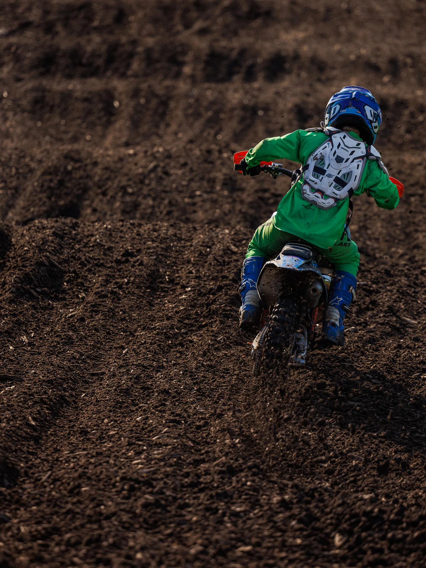 Young motocross rider on dirt bike kicking up dirt.