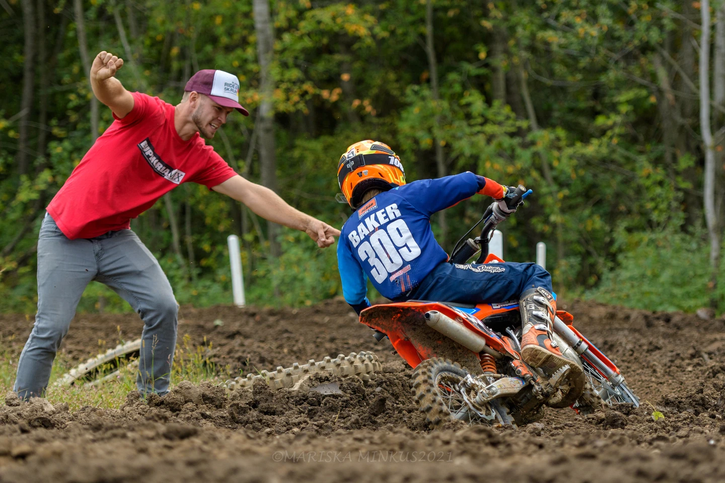 Adult cheers child on dirt bike during muddy motocross race.