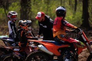Adult coaching young motocross riders on dirt bikes.